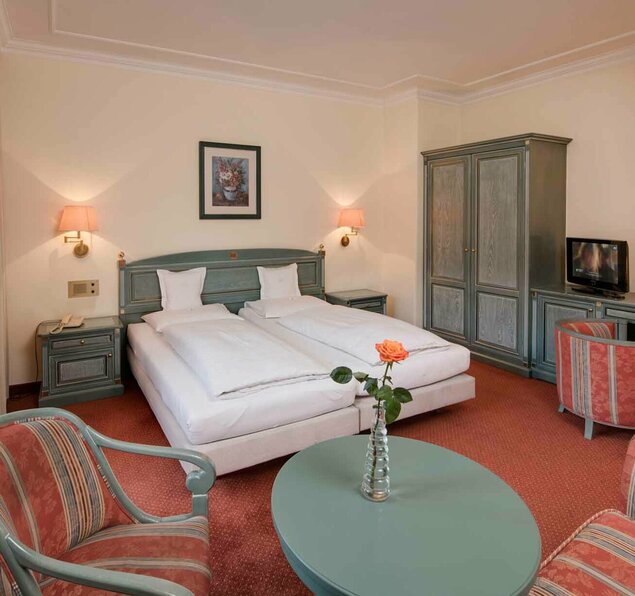 Zimmer Reschenhof Hotelbett mit Tisch und Sesseln